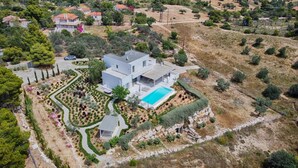 En moderne villa med swimmingpool, omgivet af anlagte haver og et kuperet landskab.