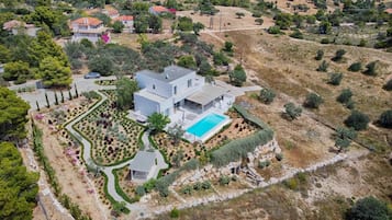 Een moderne villa met een zwembad, omgeven door aangelegde tuinen en een glooiend landschap.