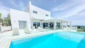 Et moderne hus med swimmingpool, udendørs siddepladser og en overdækket terrasse.