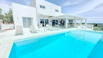 Una casa moderna con piscina, mobiliario de exterior y un patio cubierto.