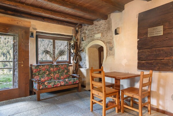 A rustic room with a wooden table and chairs, a floral sofa, and a stone wall.