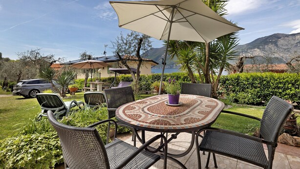 An outdoor patio with a round table, chairs, and a large umbrella. - Apartment 'Edda - Sole' with Lake View, Private Terrace, and Wi-Fi (Brenzone sul Garda)