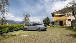 A modern two-story house with a paved driveway, a parked car, and a view of mountains in the background. - Apartment 'Edda - Sole' with Lake View, Private Terrace, and Wi-Fi (Brenzone sul Garda)