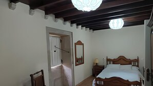 A bedroom with a wooden bed, a chair, a bedside table with a lamp, a mirror, and a ceiling light fixture. - Holiday Home 'O Lar De Natalio' with Sea View, Private Terrace and Wi-Fi (RIANXO)