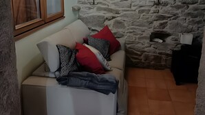 A cozy room with a stone wall, a wooden ceiling, a white sofa with patterned cushions, and a chandelier. - Holiday Home 'O Lar De Natalio' with Sea View, Private Terrace and Wi-Fi (RIANXO)