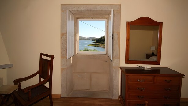 A room with a wooden chair, a dresser, and a door leading to a view of a lake. - Holiday Home 'O Lar De Natalio' with Sea View, Private Terrace and Wi-Fi (RIANXO)