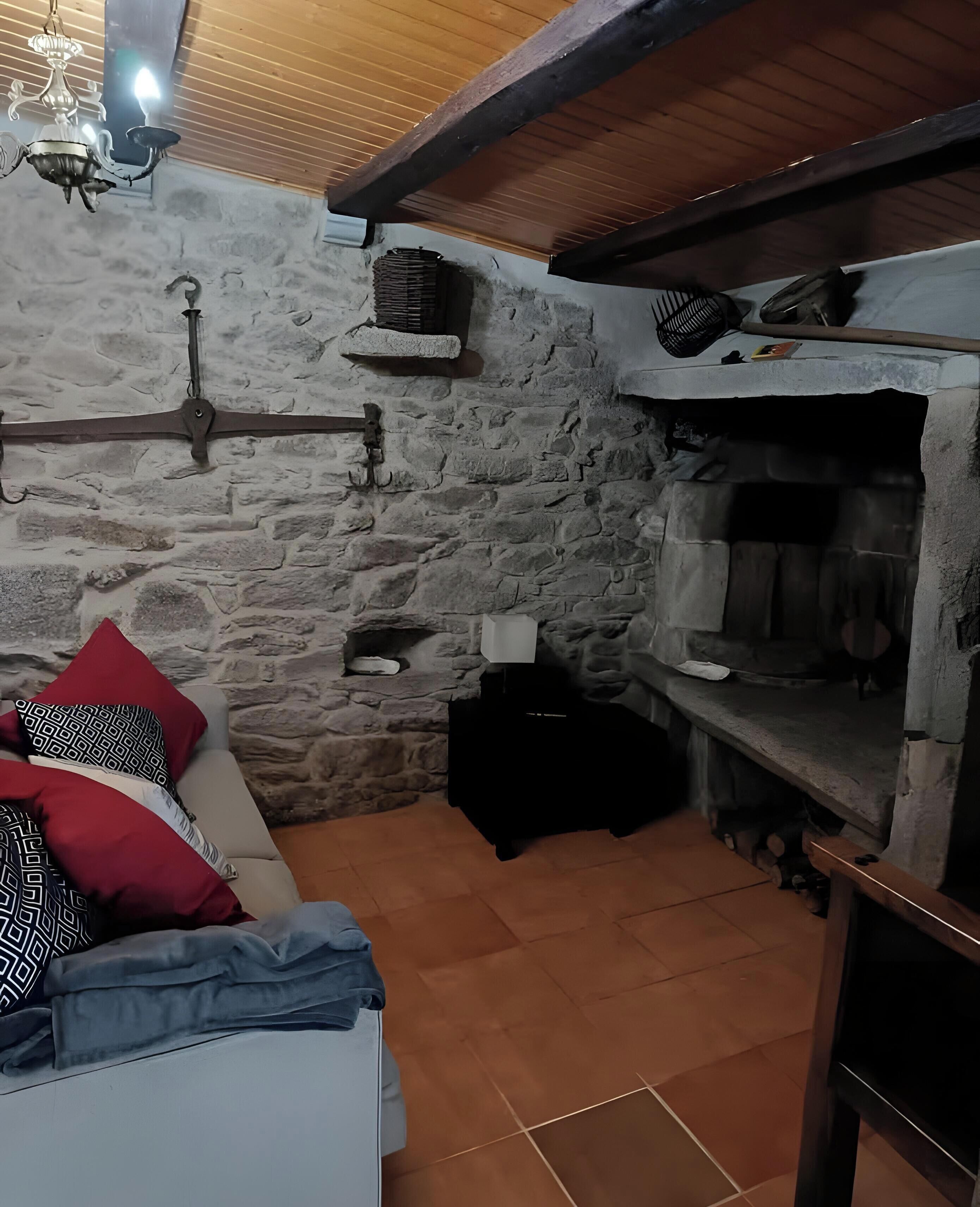Una habitación rústica con pared de piedra, chimenea, sofá con cojines estampados y techo de madera.