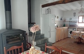 Una cocina con estufa de leña, una mesa de comedor con sillas, una escalera y una encimera con electrodomésticos.