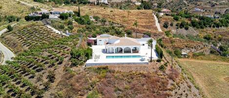 Une villa blanche avec une piscine, entourée de vignes et de collines.
