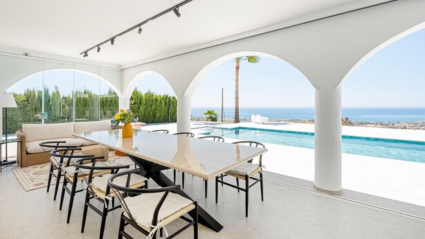 Un área de comedor exterior moderna con piscina y vista al océano.