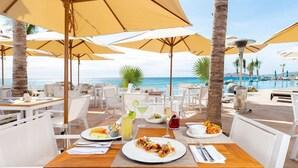 A beachside restaurant with outdoor seating, white tables, and yellow umbrellas. - Deluxe Ocean View Studio in Cabo, Villa la Valencia Resort (San José del Cabo)