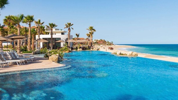A resort pool with clear blue water, surrounded by palm trees and beach views. - Deluxe Ocean View Studio in Cabo, Villa la Valencia Resort (San José del Cabo)
