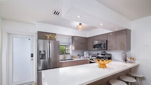 Une cuisine moderne dotée d’appareils électroménagers en acier inoxydable, d’un îlot central blanc avec des tabourets, et de meubles de rangement en bois.