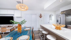 Une cuisine moderne avec des meubles blancs, un grand îlot central doté de tabourets et un téléviseur à écran plat.