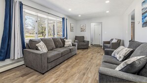 A modern living room with a grey sofa, two armchairs, and a large window with curtains.