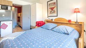 A bedroom with a bed, a red chair, a wooden headboard, a framed picture on the wall, and a small kitchenette with a microwave and refrigerator. - Lovely 4-person studio flat on the top floor with lift (Chamrousse)