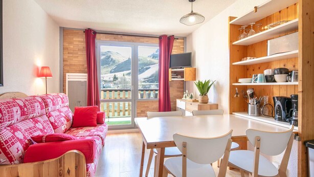 A cozy living room with a red patterned sofa, a dining table with chairs, a TV, and a kitchen area with wooden shelves. - Lovely 4-person studio flat on the top floor with lift (Chamrousse)