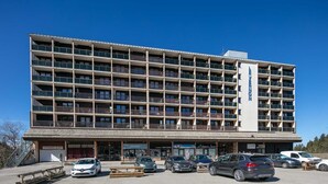 A multi-story hotel with balconies, a parking lot, and several storefronts. - Lovely 4-person studio flat on the top floor with lift (Chamrousse)