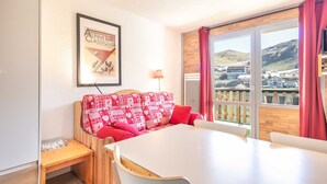 A room with a white table, red patterned sofa, and a framed picture on the wall. - Lovely 4-person studio flat on the top floor with lift (Chamrousse)
