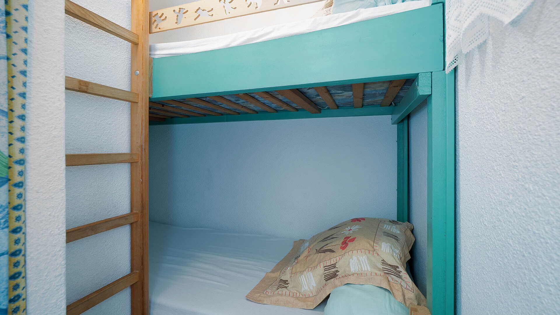 A bunk bed with a ladder, a single bed with a patterned blanket, and a white wall.