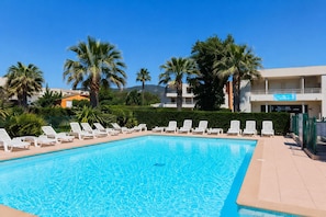 A rectangular swimming pool with clear blue water, surrounded by white lounge chairs.