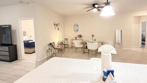 A modern living room with a large white rug, a ceiling fan, and a dining area with a table and chairs. - 3BR | Spacious | Entire House | Close to all Parks (Orlando)