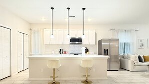 A modern kitchen with white cabinets, a central island with stools, stainless steel appliances, and pendant lighting. - 3BR | Spacious | Entire House | Close to all Parks (Orlando)