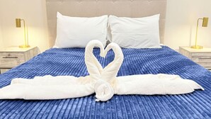 A bed with a blue textured bedspread, two white pillows, and a towel arranged in a heart shape on the bed. - 3BR | Spacious | Entire House | Close to all Parks (Orlando)