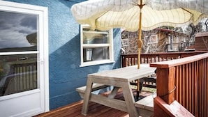 Eine Holzterrasse mit Tisch und Sonnenschirm, ein Fenster mit weißem Rahmen und eine blaue Wand.