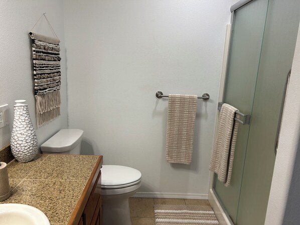 Un baño con inodoro, lavamanos, ducha y toallas colgadas en la pared.