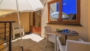 Un balcon avec un parasol blanc, des chaises en osier, une petite table avec des bols, et une fenêtre donnant sur un immeuble.