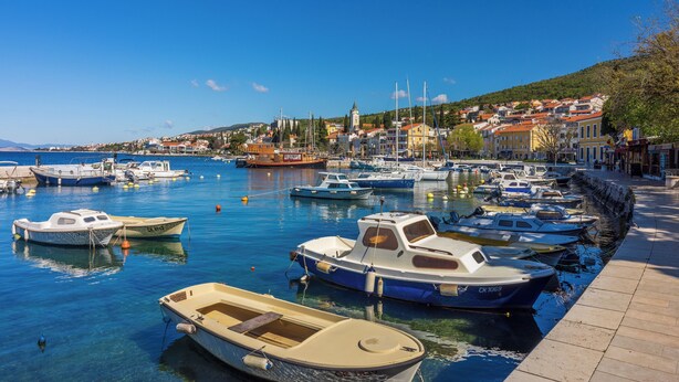 Un port de plaisance où sont amarrés différents types de bateaux, un ciel bleu dégagé et des bâtiments en arrière-plan.