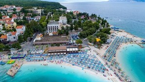 Vue aérienne d’une ville côtière avec un hôtel, une plage et des eaux d’un bleu limpide.