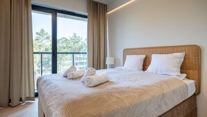 Ein Hotelzimmer mit einem großen Bett, beigen Vorhängen und Blick auf Bäume durch das Fenster.