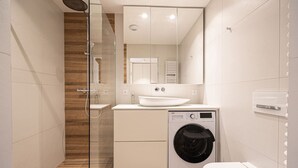 Ein modernes Badezimmer mit Duschkabine aus Glas, einer integrierten Waschmaschine und einem weißen Waschbecken.