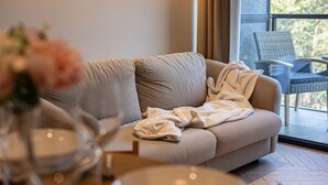 Ein modernes Wohnzimmer mit einem beigen Sofa, einem Glastisch und Blick auf Grün durch ein großes Fenster.