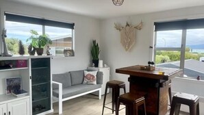 A modern living room with a grey sofa, a wooden bar table, and a large window offering a view of the outdoors.