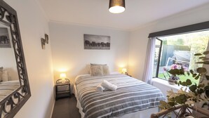 A bedroom with a bed, bedside tables, a mirror, a window with a view of the garden, and a painting on the wall.
