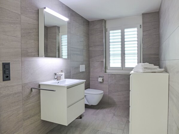 A modern bathroom with a white sink, toilet, and a mirror above the sink.
