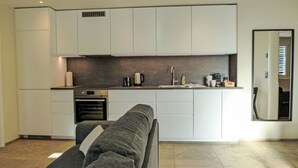 A modern kitchen with white cabinets, a built-in oven, and a countertop with a kettle and coffee maker. - Huus Chloster, Apt Niesen by Interhome (Krattigen)