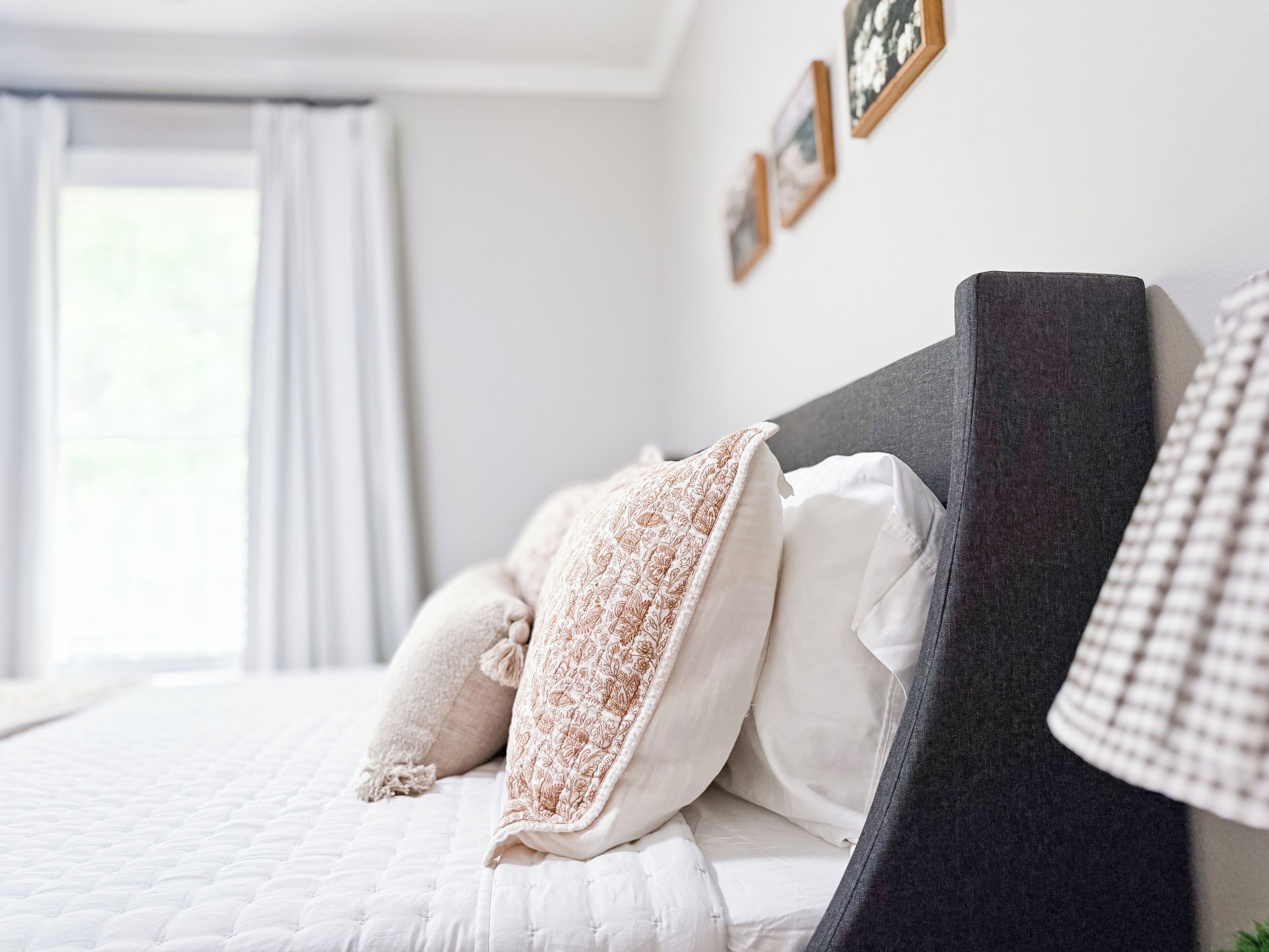 A neatly made bed with pillows and a blanket, a dark headboard, and a window with curtains.