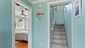 Un couloir aux murs bleu clair, doté d’un plancher en bois et d’un escalier menant à une autre pièce.