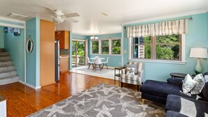 Un vaste salon agrémenté d’un grand tapis gris à motifs d’étoiles de mer, d’un canapé bleu foncé et d’un coin repas avec des chaises blanches.