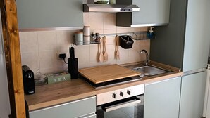 Eine kompakte Küche mit Gasherd, Backofen und Spüle. Es gibt Schränke, eine Arbeitsplatte und eine Spritzschutzwand.