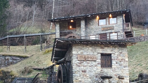 Ein aus Stein gebautes Gebäude namens 'MULINO' mit Wasserrad, Holzboden und Lichterketten.