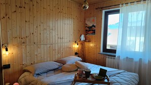 Ein Zimmer in einer Holzhütte mit einem Bett, einem Nachttisch, einer Lampe und einem Fenster mit Vorhängen.