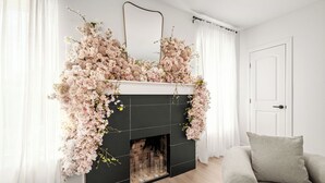 A fireplace with floral decorations, a white door, and a grey sofa in a room with light wooden flooring. - 2 Linked Suites • 6BR/6BA • Heated Pool/Spa • BBQ (Houston)