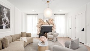 A modern living room with a sofa, armchair, and coffee table. There is a fireplace with floral decorations and a hanging light fixture. - 2 Linked Suites • 6BR/6BA • Heated Pool/Spa • BBQ (Houston)
