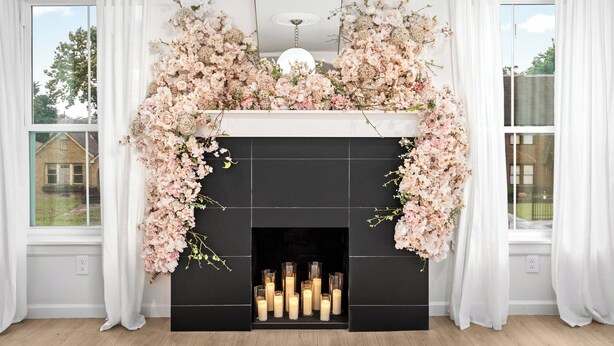 A fireplace with a floral arrangement above it, a mirror above the fireplace, and a view of a house through the window to the left. - 2 Linked Suites • 6BR/6BA • Heated Pool/Spa • BBQ (Houston)