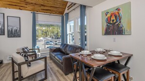 Un coin repas avec une table en bois dressée pour quatre personnes, un canapé en cuir marron et un tableau encadré accroché au mur.